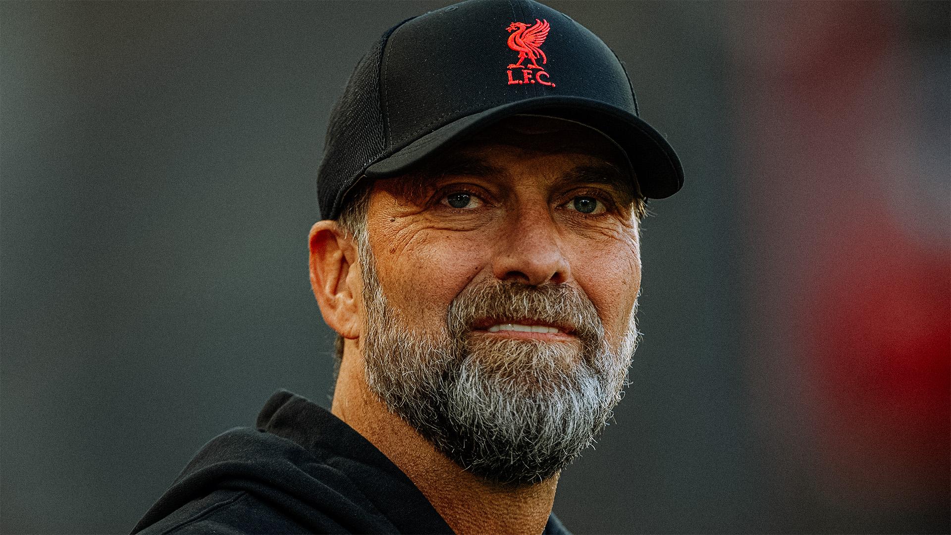 Klopp trener Liverpoola najavljuje utakmicu Lige prvaka u utorak u 21 sat na fotografiji Jurgen Klopp u crnoj dukserici i crnom kačketu vidi se samo do ramena osmijeh na licu preplauo ten brada prosijeda na kapi znak Liverpoola crvena ptica i LFC siva pozadina fotografije