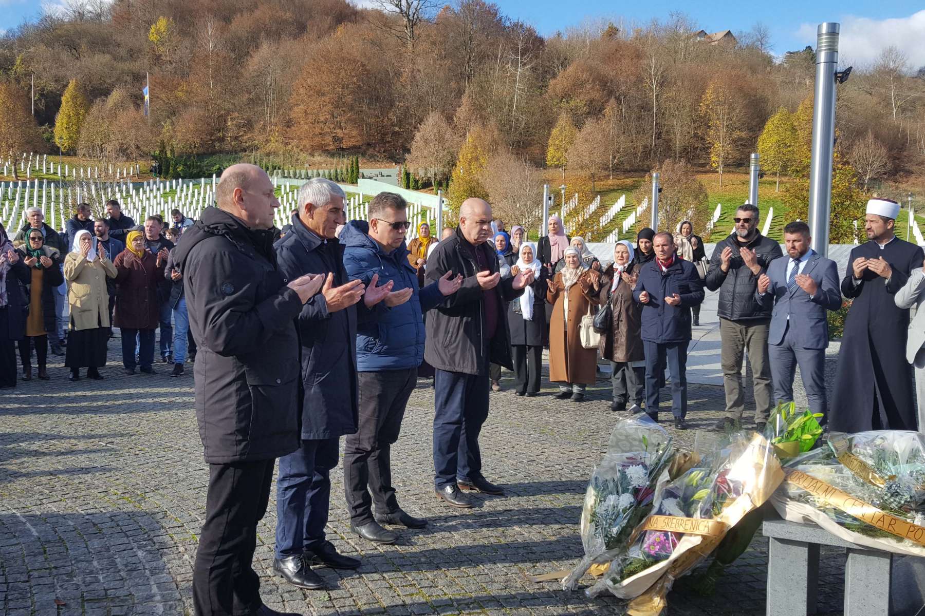 U Memorijalnom centru Potočari obilježen Dan državnosti BiH ljjudi uče Fatihu na mezarju pored spomenika vidi se tridesetak ljudi sa podignutim rukama dok izgovaraju molitvu cvijeće pred spomenikom iza mezarje sunčan dan