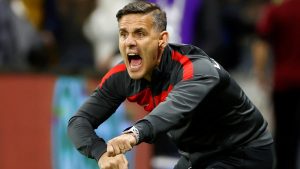 Kanadski selektor John Herdman sageo se u crnoj trenirci sa crvenom trakom od ramena do kraja rukava na lijevoj ruci sat izraz lica govori kao da sa klupe glasno dovikuje nekome nešto iza publika