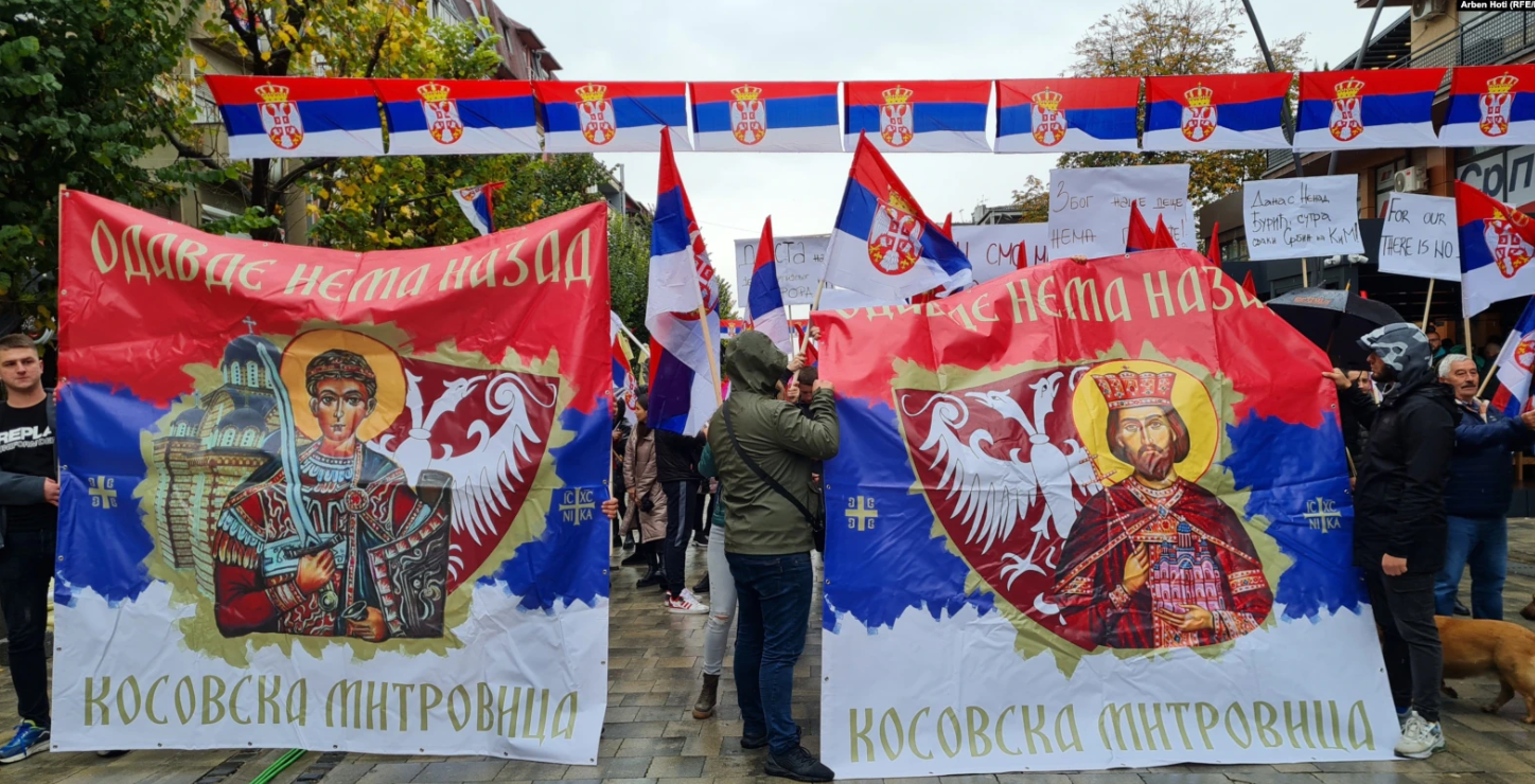 protest Srba u Sjevernoj Mitrovici protest na Kosovu srpske zastave sa orlovima na njima piše odavde nema nazad na ćirilici ljudi drže transparente na sredini muškarac u jakni sa kapuljaćom na glavi ne vidi se lice oblačan dan