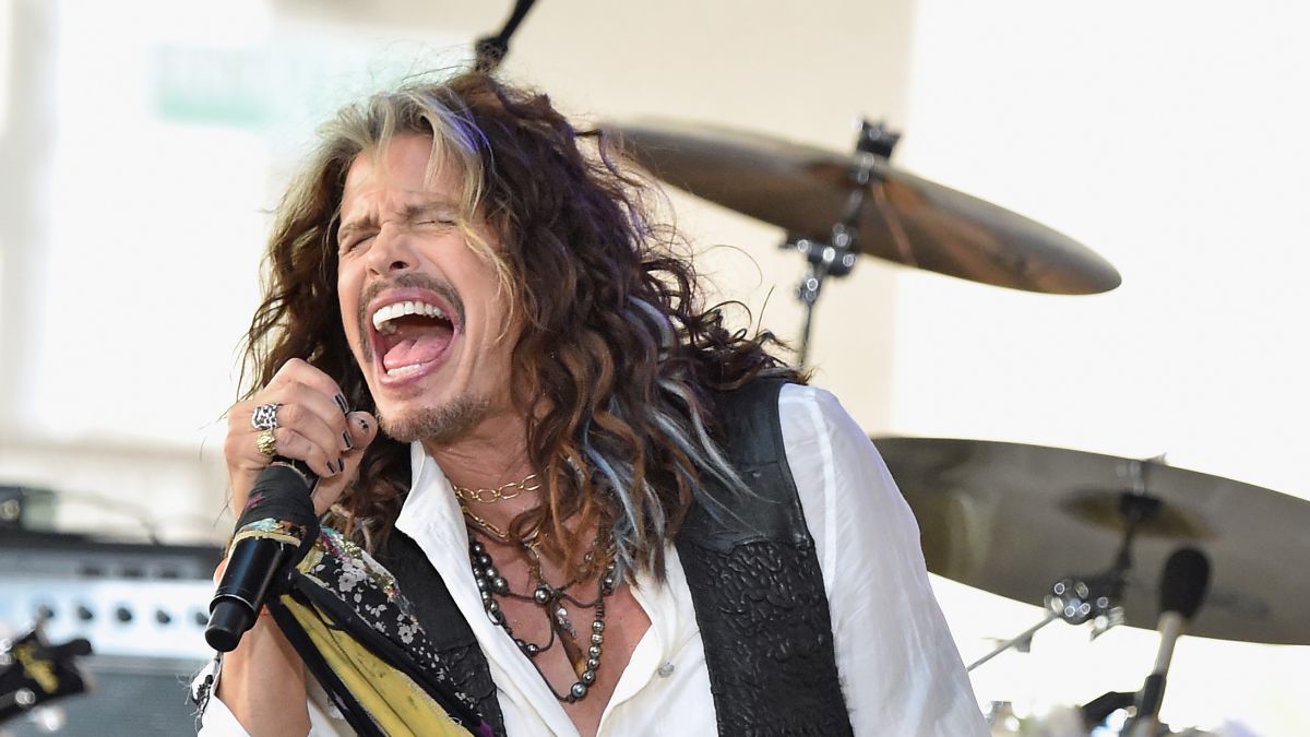 'misteriozne' bolesti Steven Tyler pjeva na pozornici u bijeloj košulji crniprsluk duga kosa bubnjevi iza