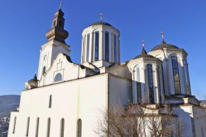 Pokradena Saborna crkva Saborna crkva u Mostaru bijelo veliko zdanje sa tri kule i jednim zvonikom na prednjem zidu šest prozora drvo uz desnu stranu crkva plavo nebo bez oblaka dan